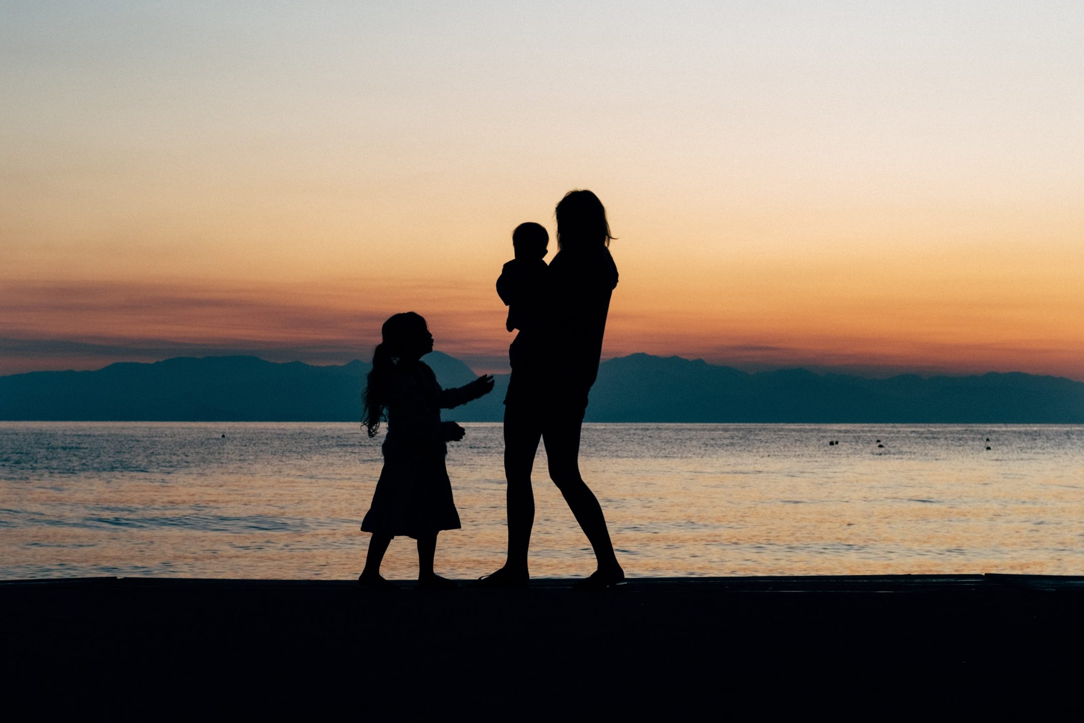 Silhouette of mother, baby and young child on beach at sunset