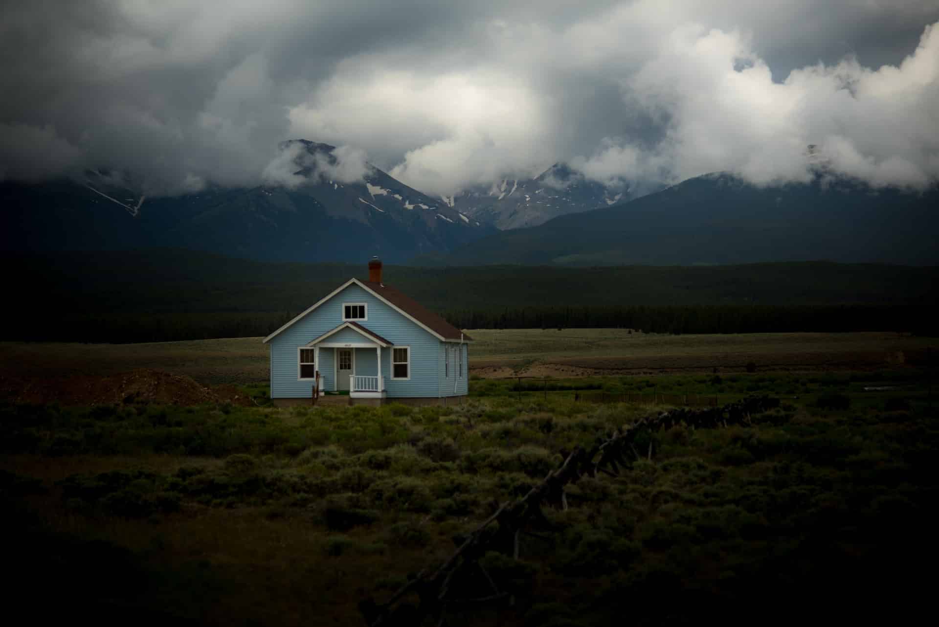 A small blue house on a wide expanse of empty property with mountains in the background, representing estate trustees, executors, and the rule against self-dealing