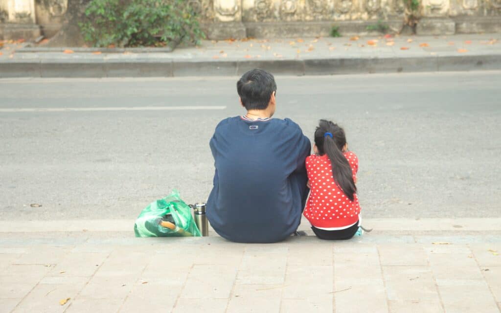 A father and daughter sitting on a curb at side of road