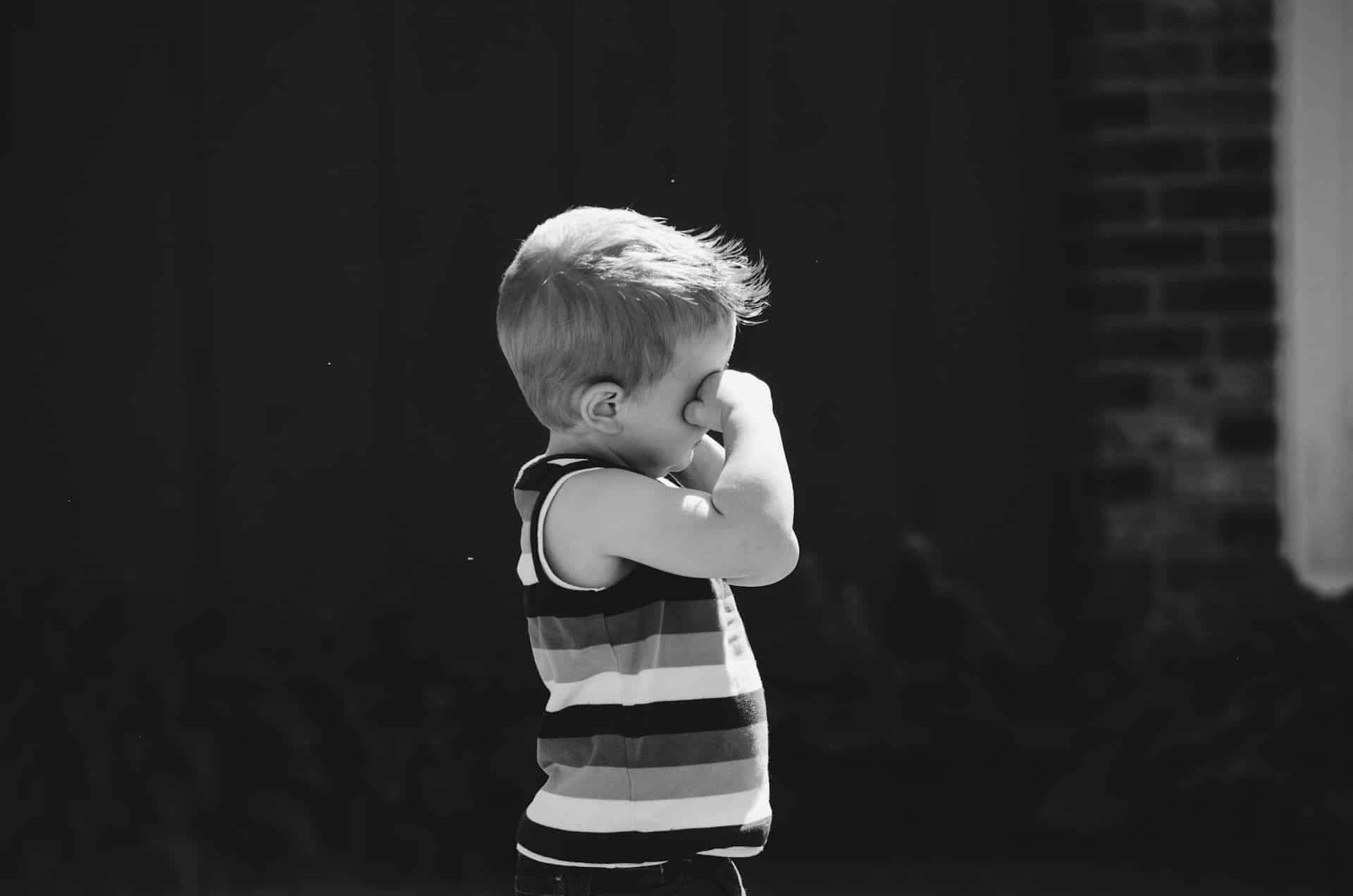 grayscale photo of a boy rubbing his eyes