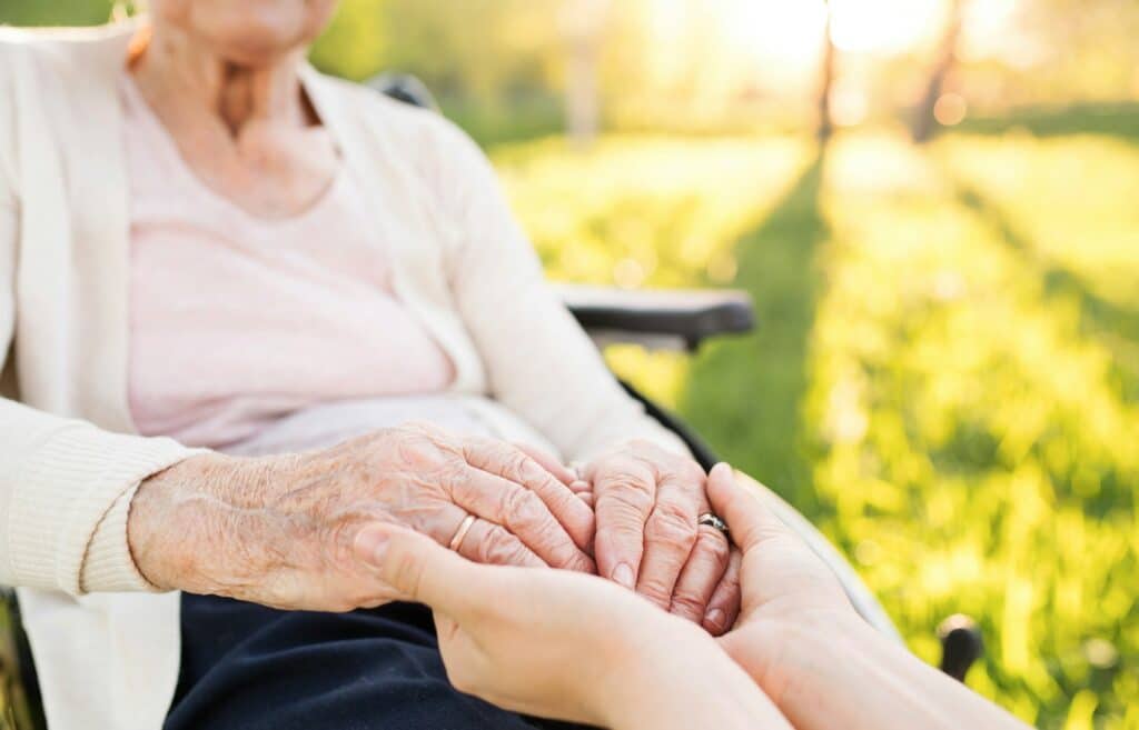An elderly woman in a wheelchair holding hands with a younger person, representing committeeship.