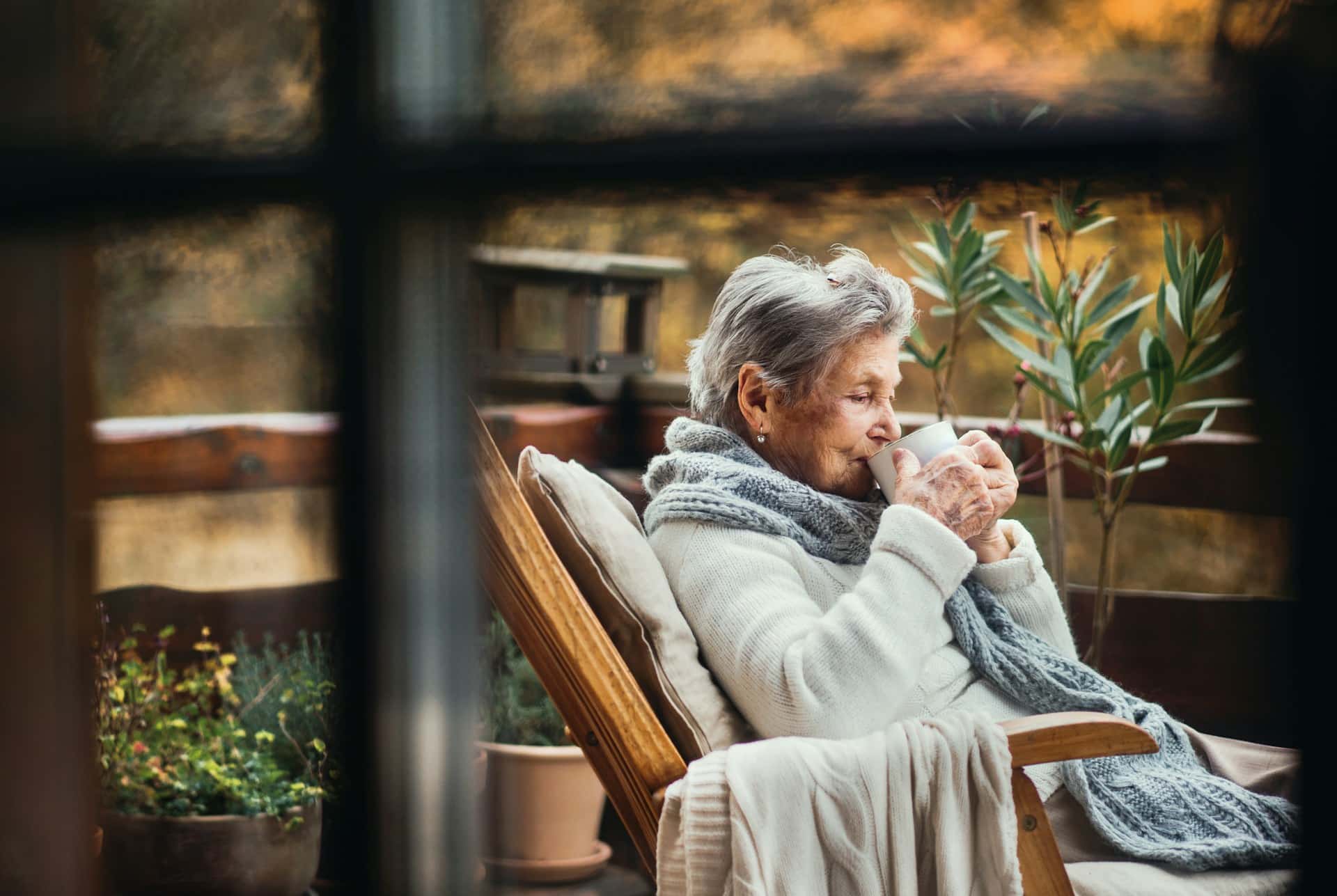 An elderly woman drinking coffee outdoors through a window, representing power of attorney abuse.