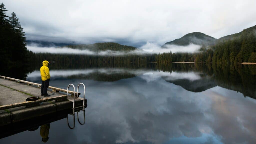 A man fishing from a dock on a smooth, misty lake, representing riparian rights.