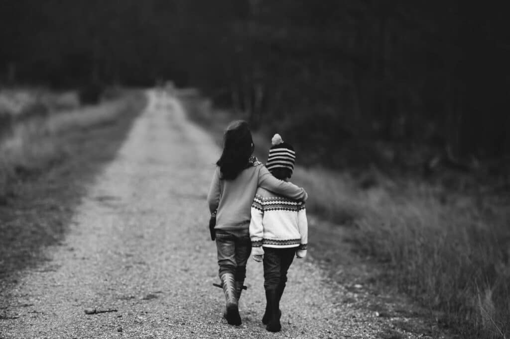 View from behind of two children walking down a gravel road, with an older girl with her arm around a younger boy’s shoulders, representing witness credibility in contentious family and parenting disputes.
