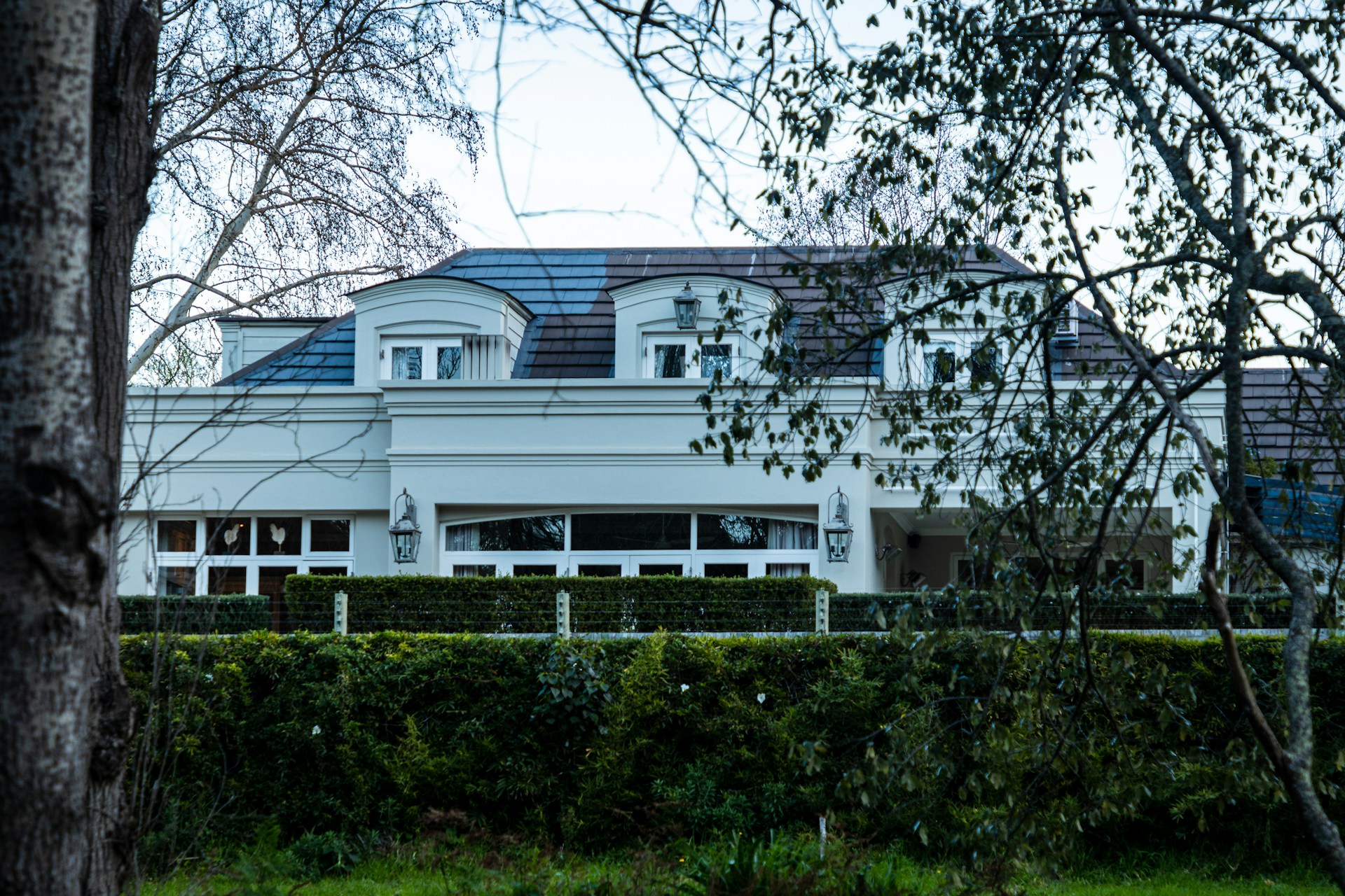 A large while house with three dormer windows and a black roof behind a lush green hedge and trees in the foreground, representing Property Division.