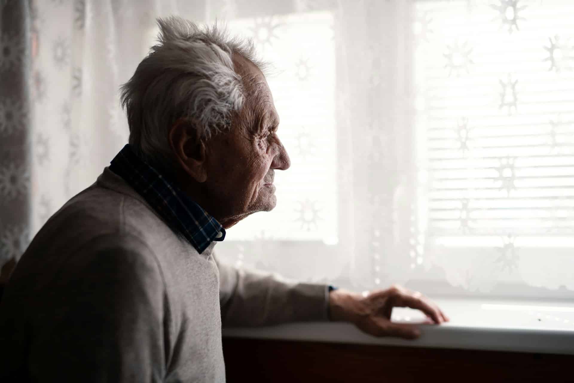 The profile of an elderly man, looking longingly out a window, veiled with a lacey curtain, representing age discrimination in BC.