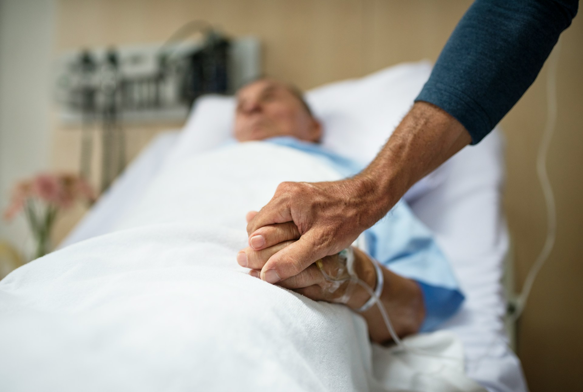 An elderly man in a hospital bed holds his son's hand, representing will revocation and intestacy.