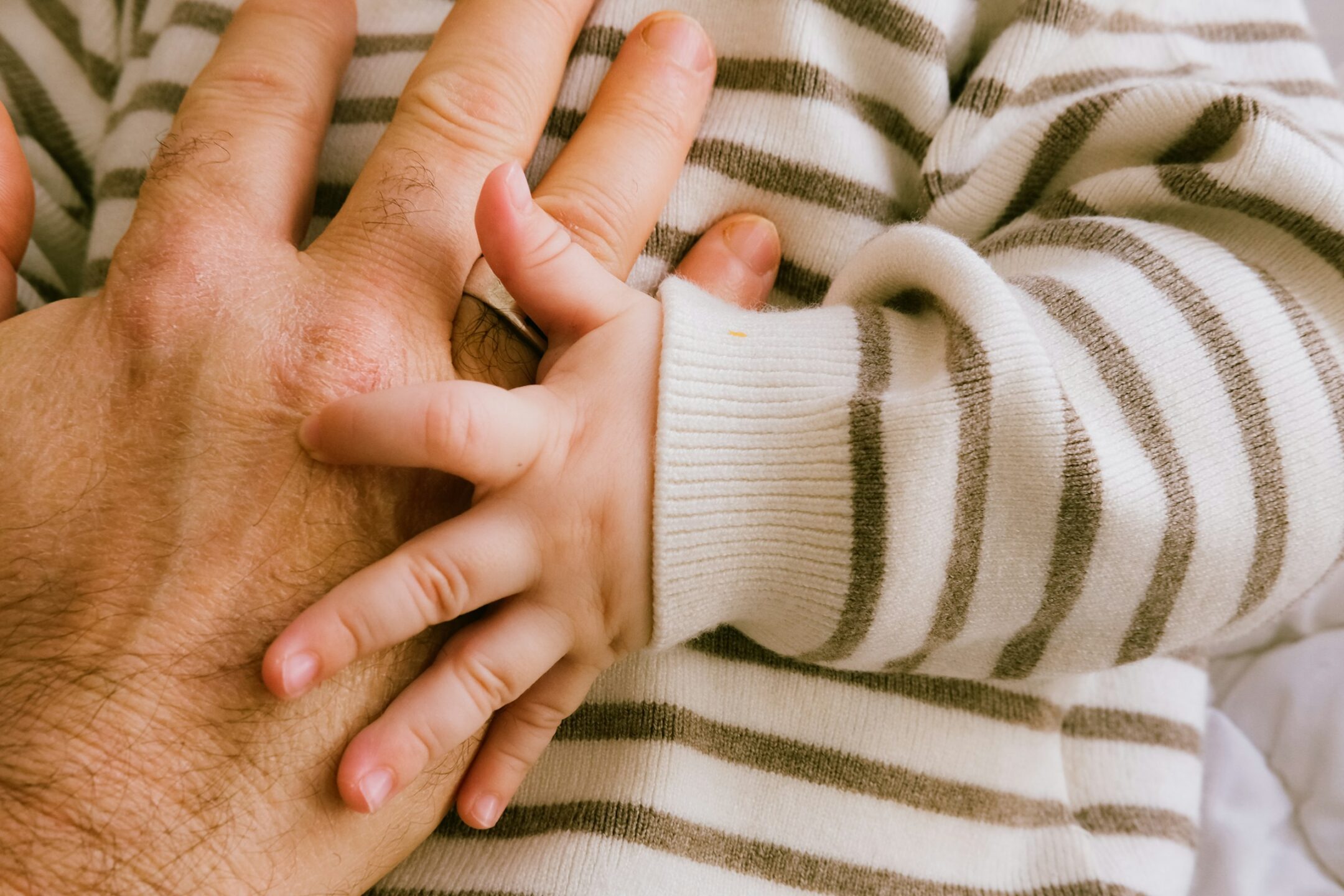 Close-up of an adult's hand holding a small baby's hand, representing wills variation claims and dependant support obligations under B.C. estate law, and the will dispute lawyers at Meridian Law Group in Vancouver.