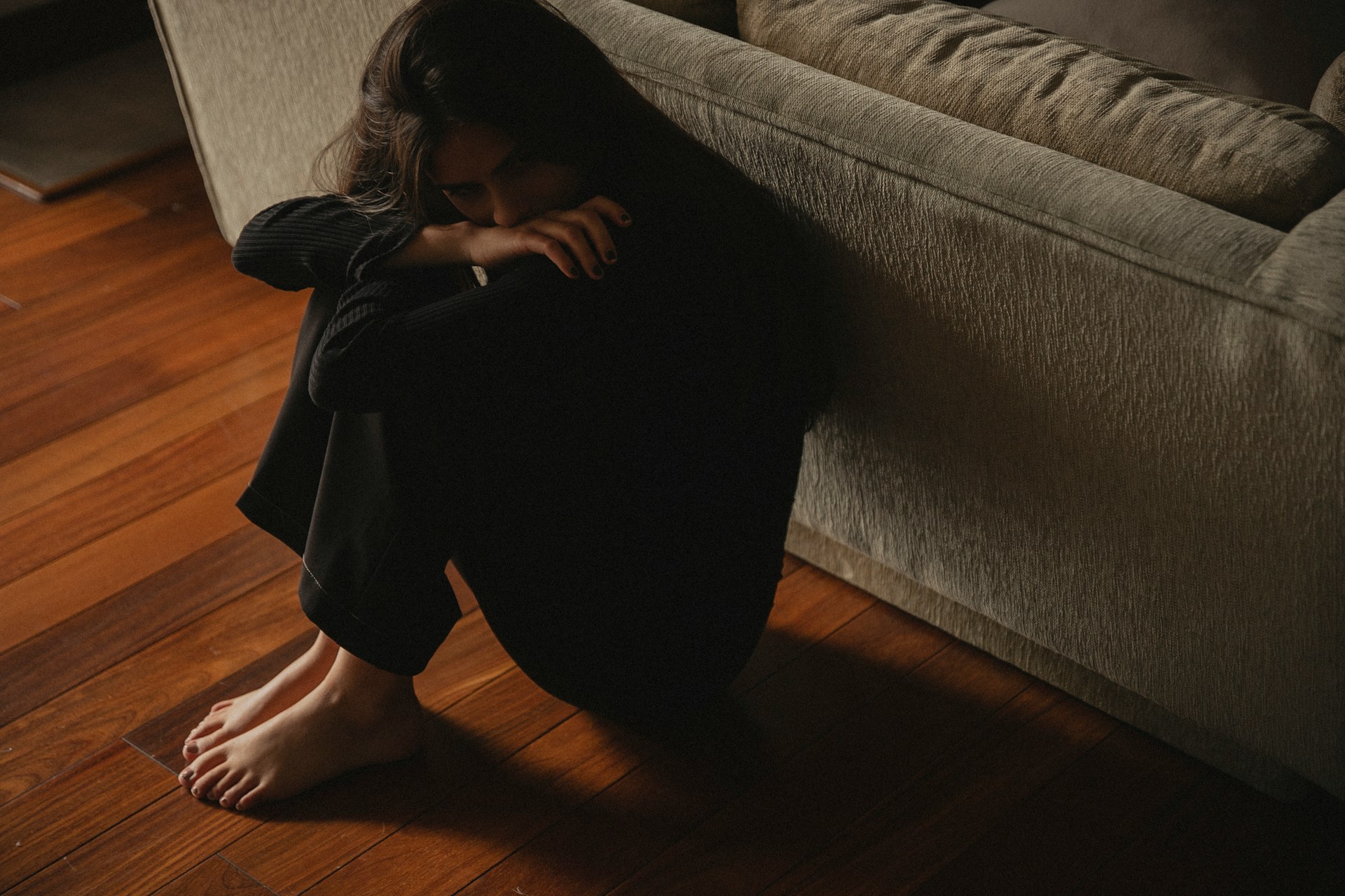 A woman sitting on the floor with her back against a couch, with her head in her hands, representing the tort of intimate partner violence in Canada and the family and divorce lawyers at Meridian Law Group in Vancouver, B.C.