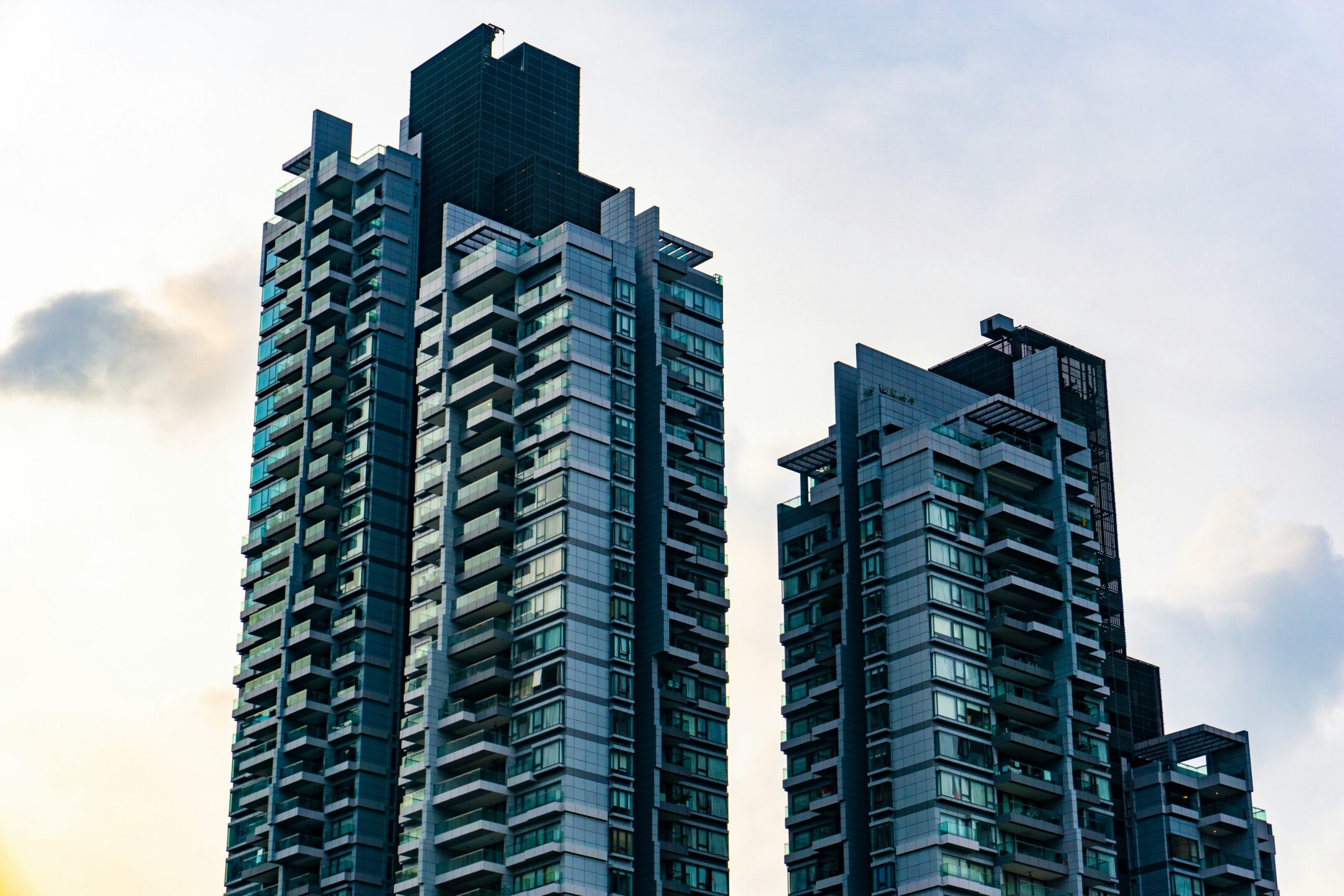 Two high-rise condominium buildings against a pale blue sky and the dull sun reflecting from the windows, representing condo value increase and separation in BC.