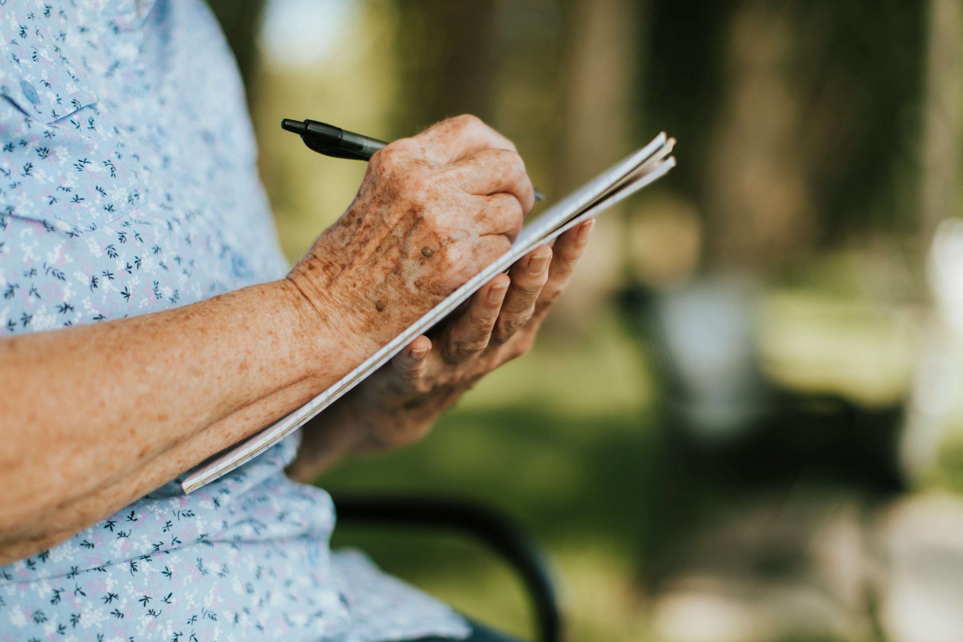 An elderly person holding a pen and notepad representing handwritten wills.