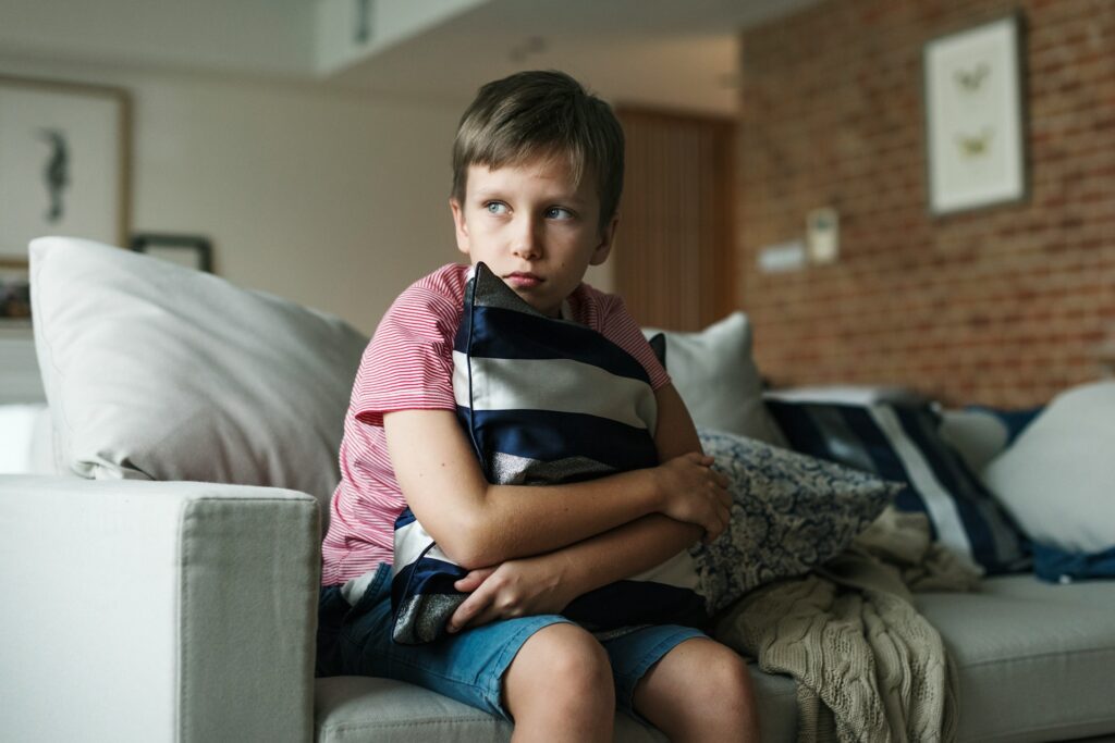 A young boy sits on the sofa, clutching a striped throw pillow to his chest, representing Views of the Child Reports.