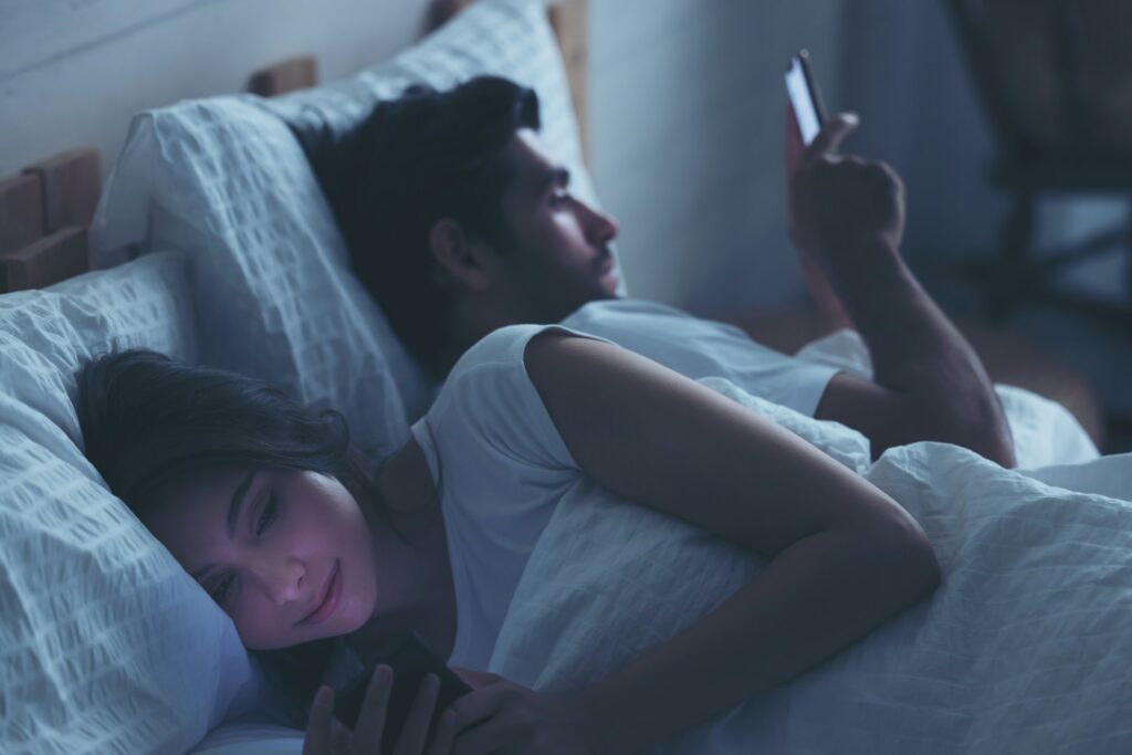 A couple in bed looking at their cell phones, representing adultery and spousal support.