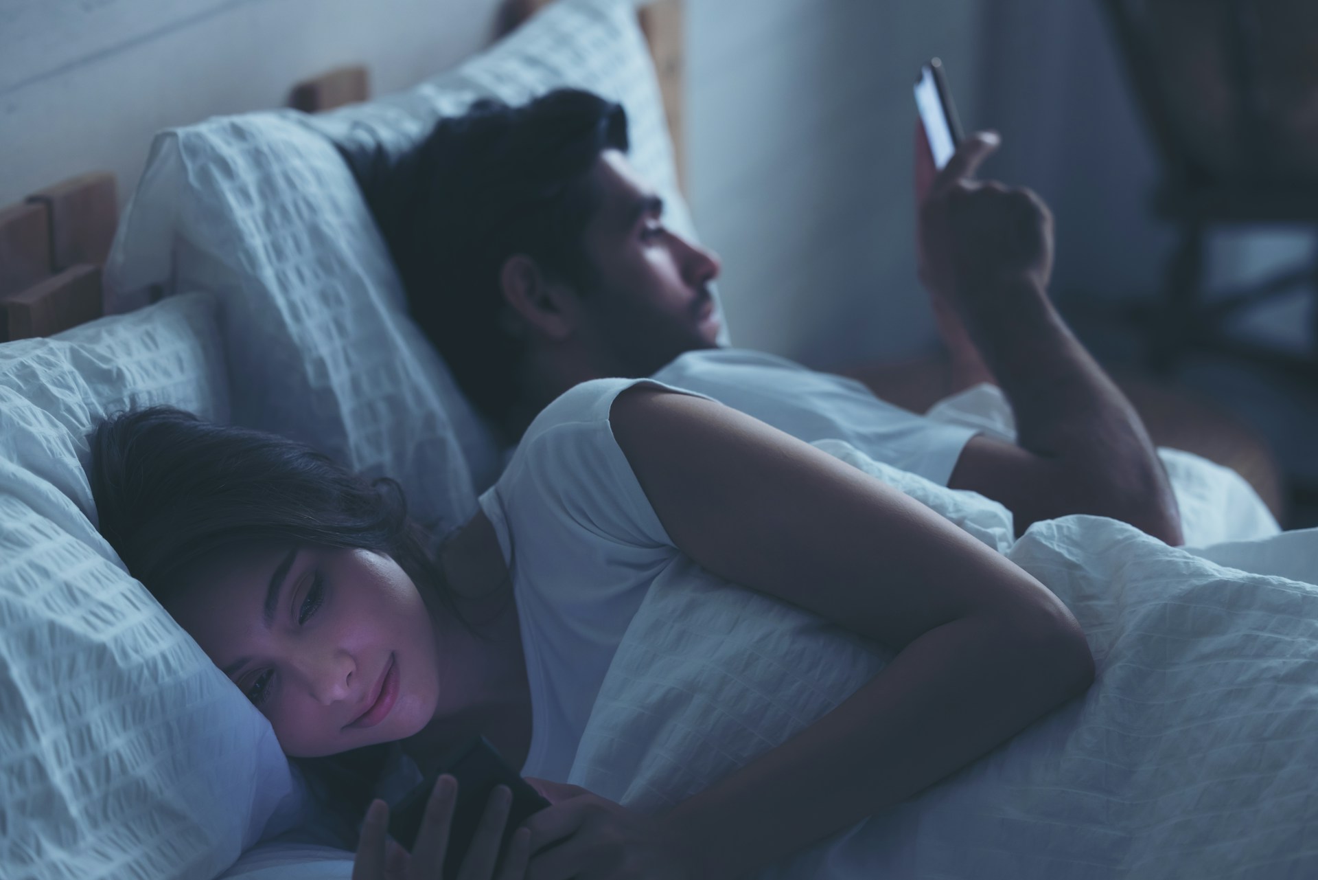 A couple in bed looking at their cell phones, representing adultery and spousal support.