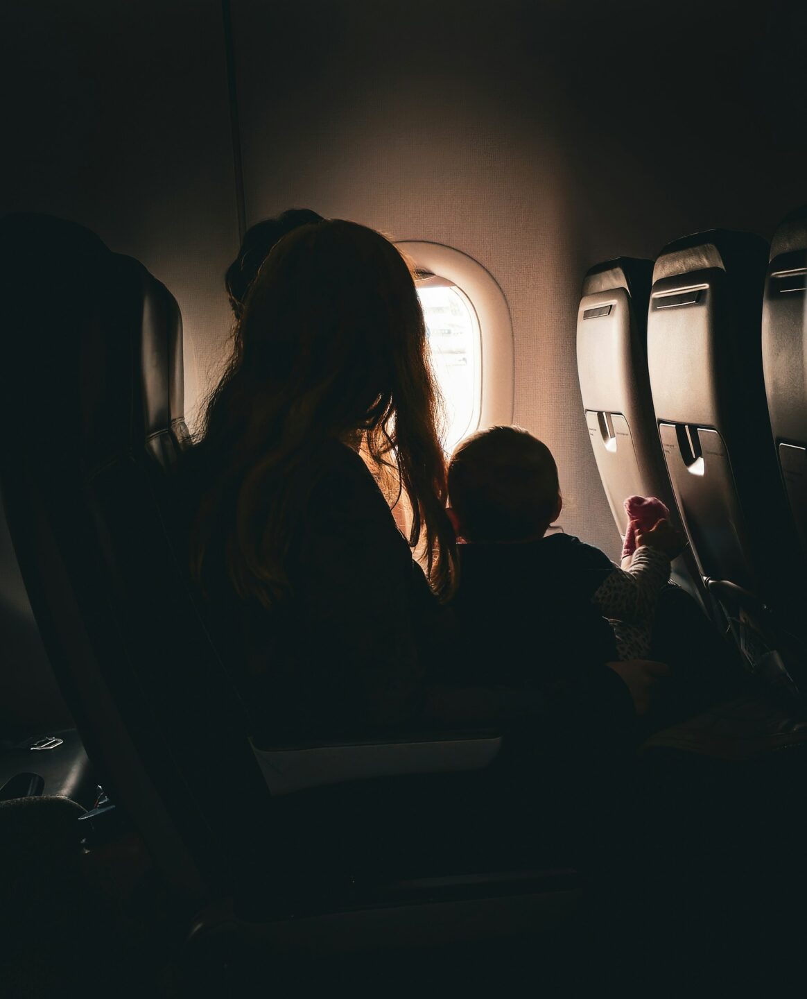 A woman with a baby on her lap faces the window on an airplane, representing child relocation in BC.