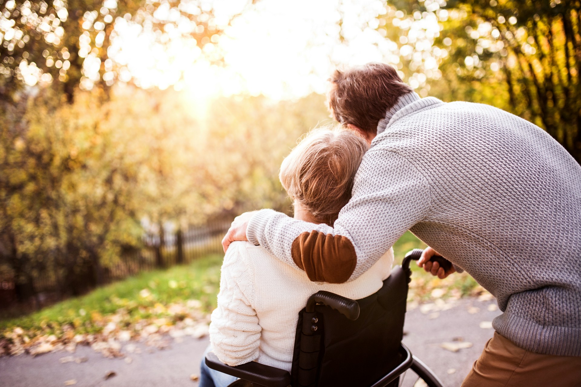 A person sitting in a wheelcair with a man holding her shoulder looking at the sunset, representing power of attorney and committeeship in BC
